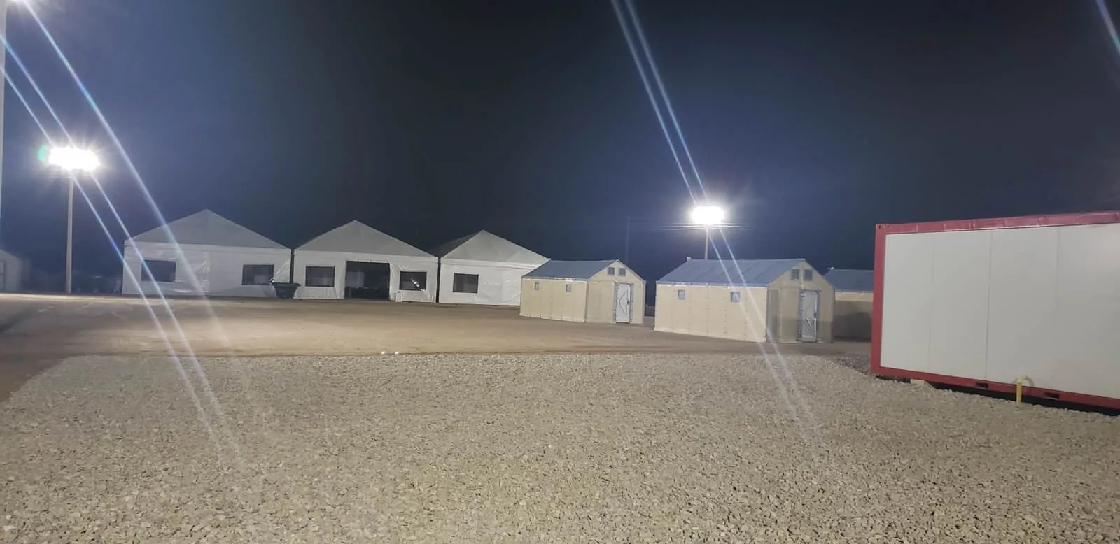 Campamento temporal nocturno con carpas y módulos operativos
